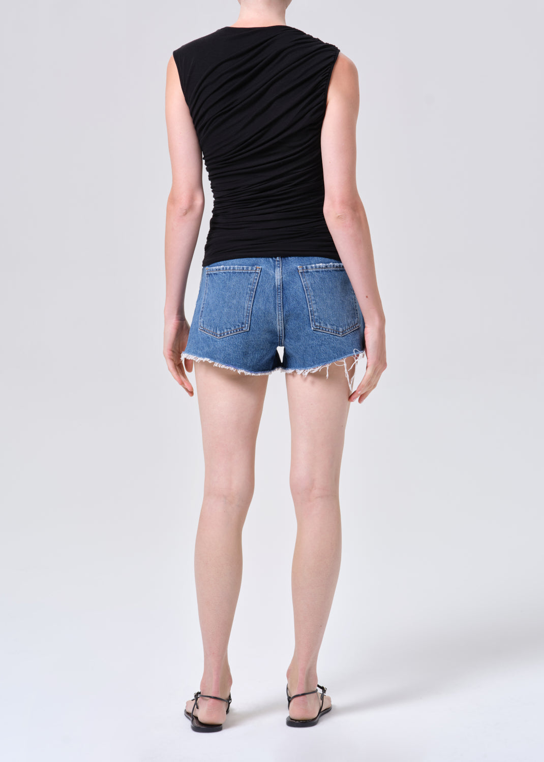 Person wearing a black sleeveless top and blue denim shorts on a white background