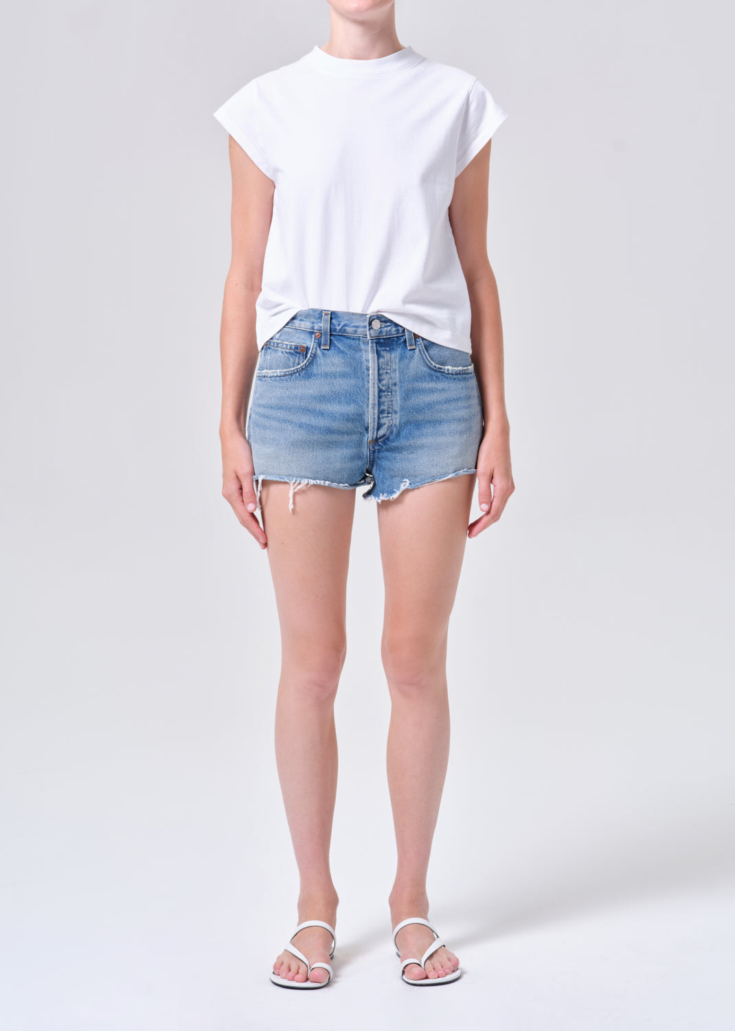 Person wearing a white t-shirt and light blue denim shorts on a plain background