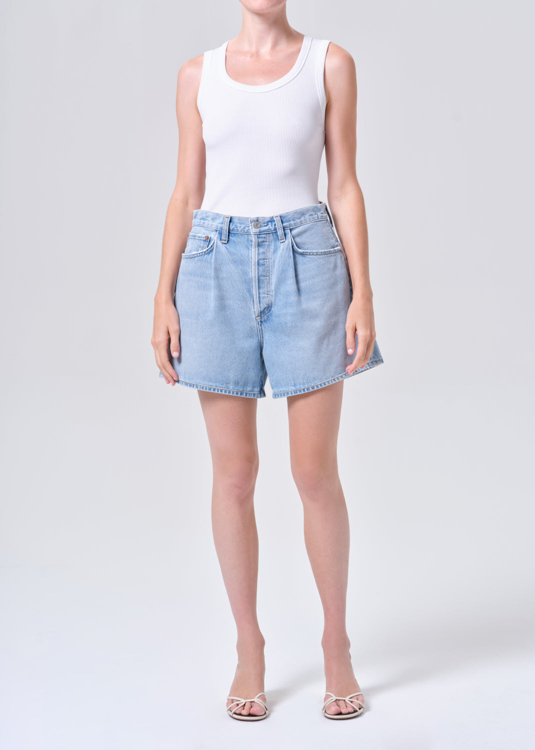 Person wearing a white tank top and light blue denim shorts on a white background
