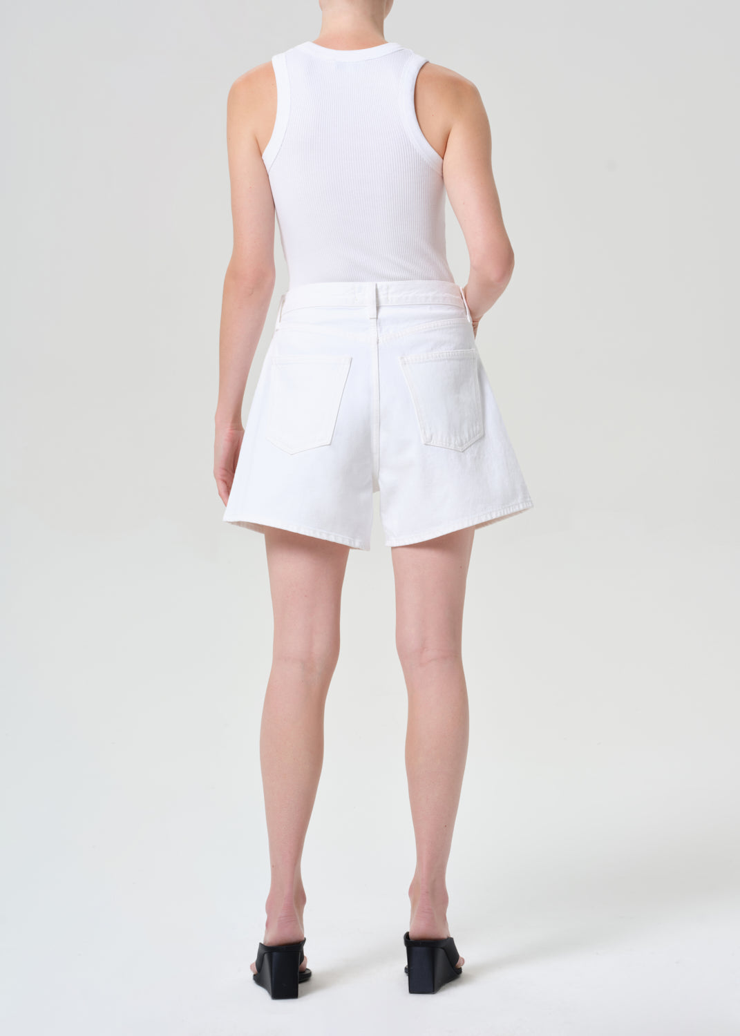 Person wearing a white sleeveless top and shorts on a plain background
