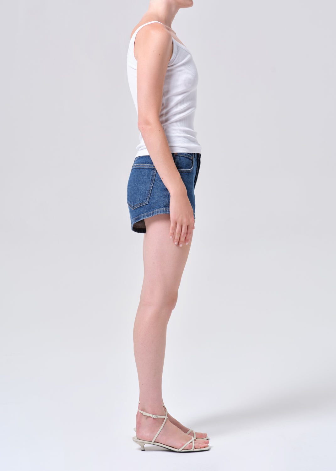 Person wearing a white tank top and blue denim shorts on a plain background
