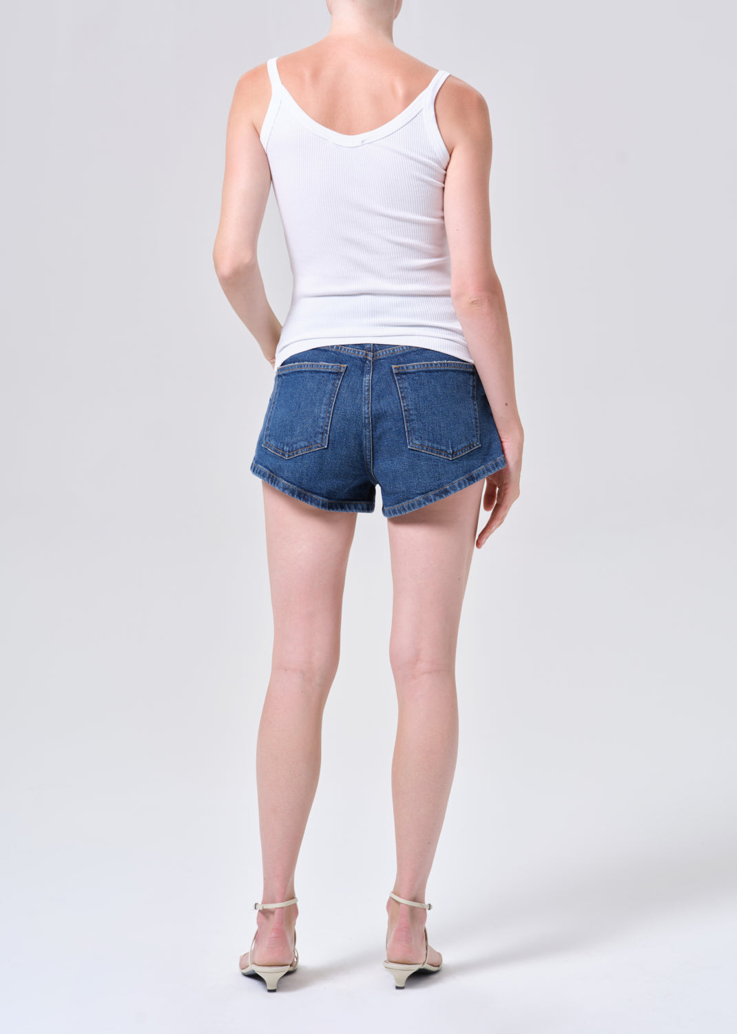 Person wearing a white tank top and blue denim shorts on a plain background