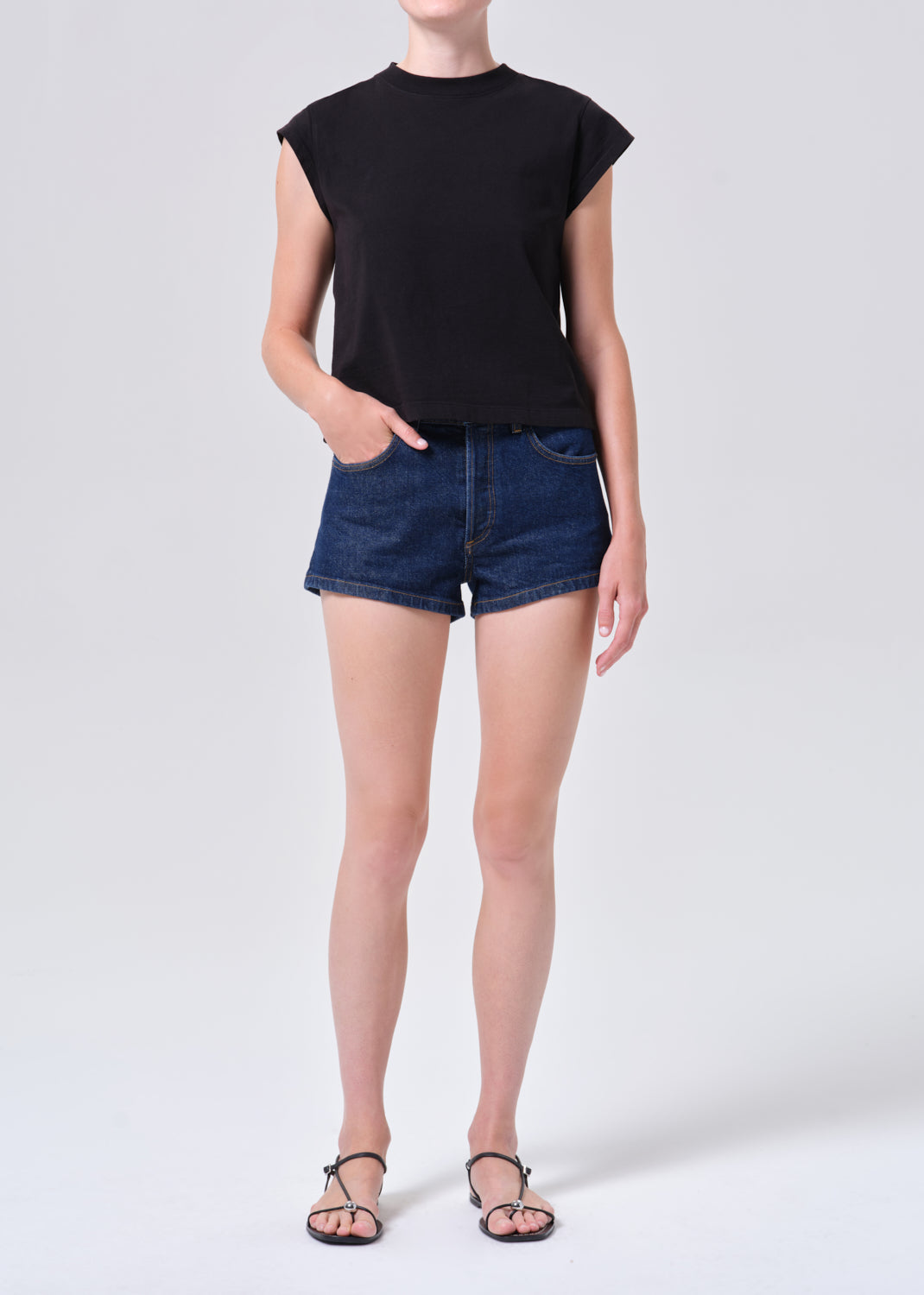 Person wearing a black sleeveless top and blue denim shorts on a white background