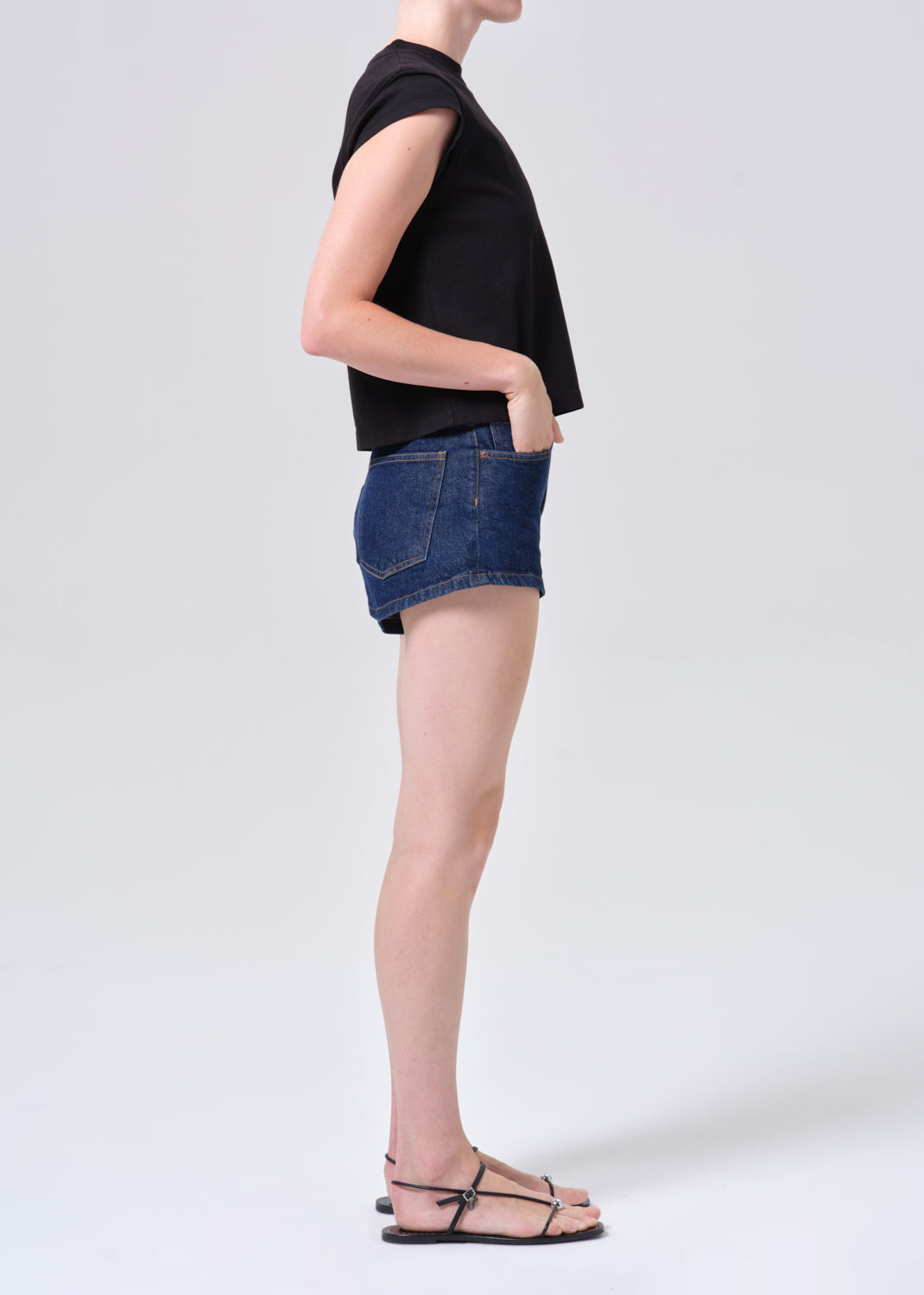 Person wearing a black sleeveless top and blue denim shorts on a white background