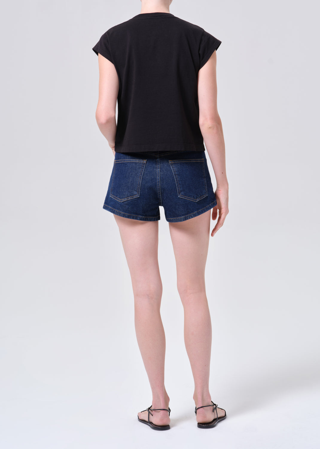 Person wearing a black sleeveless top and blue denim shorts on a white background