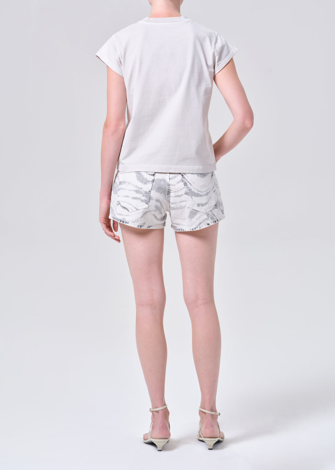 Person wearing a white t-shirt and light-colored shorts on a plain background