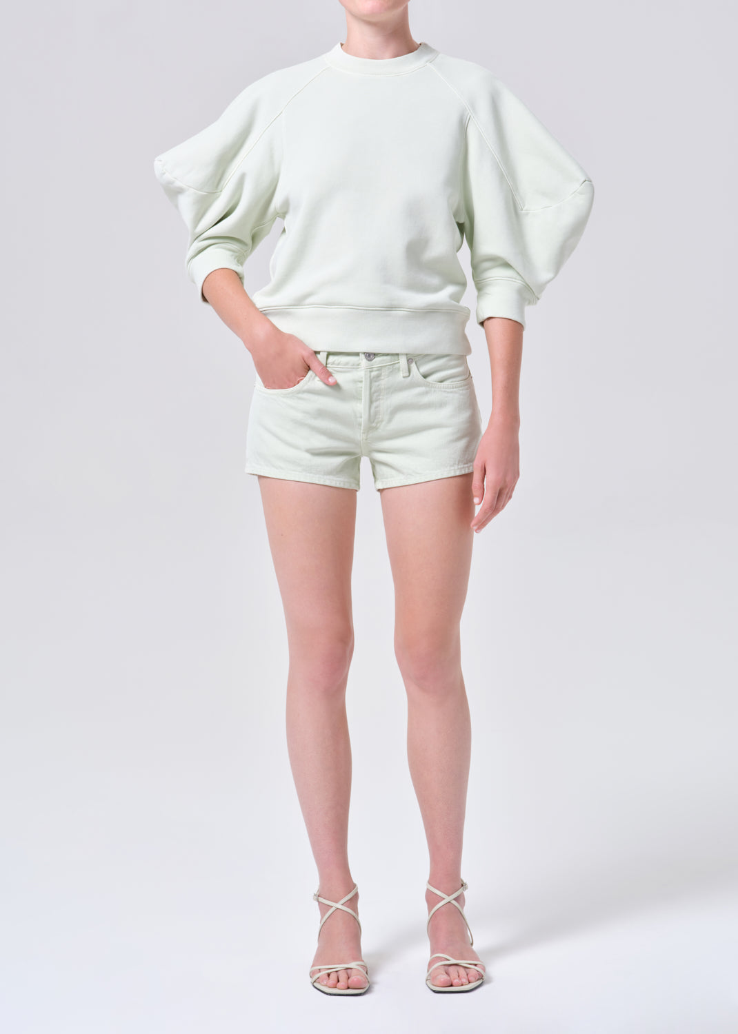 Person wearing a light green sweater and shorts on a white background