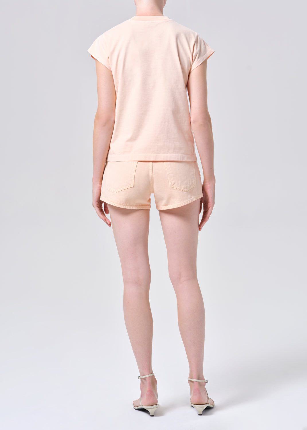 Person wearing a light pink outfit with shorts on a white background