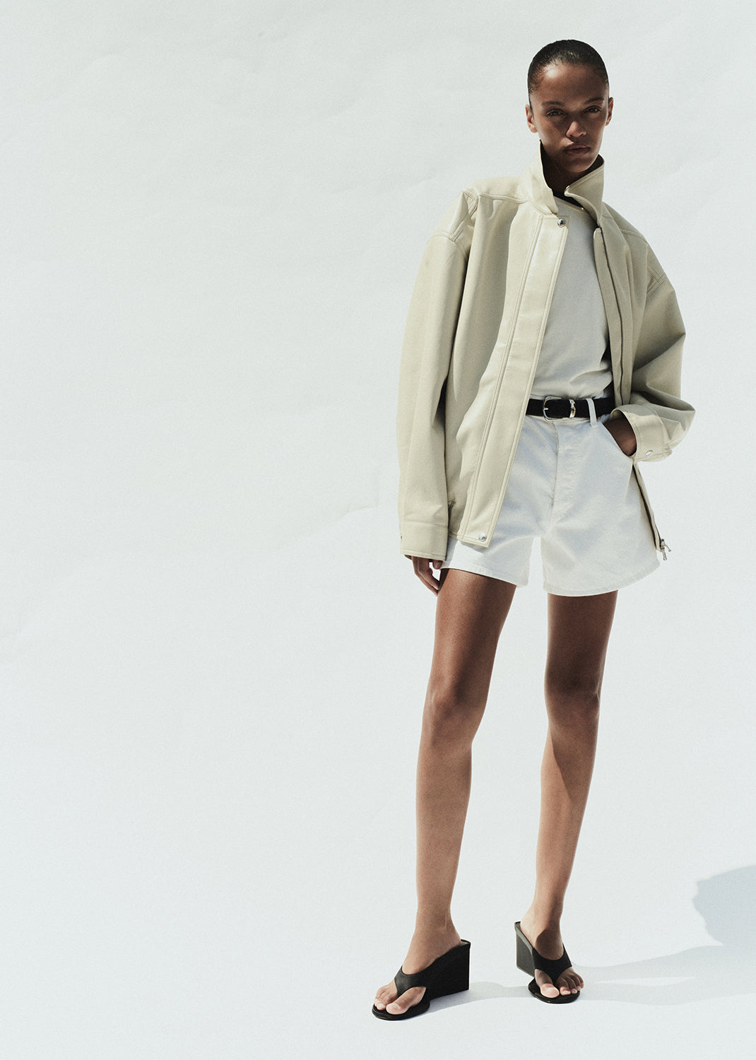 Person wearing a beige jacket and white shorts on a white background