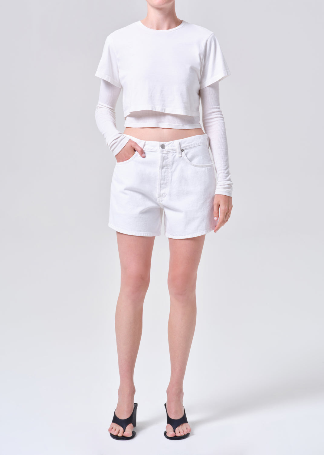 Person wearing a white long-sleeve crop top and white shorts on a plain background