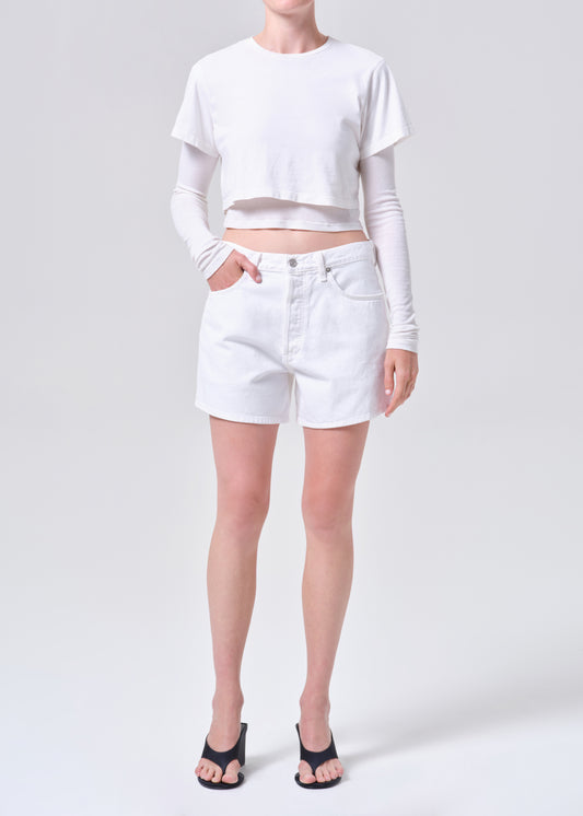 Person wearing a white long-sleeve crop top and white shorts on a plain background