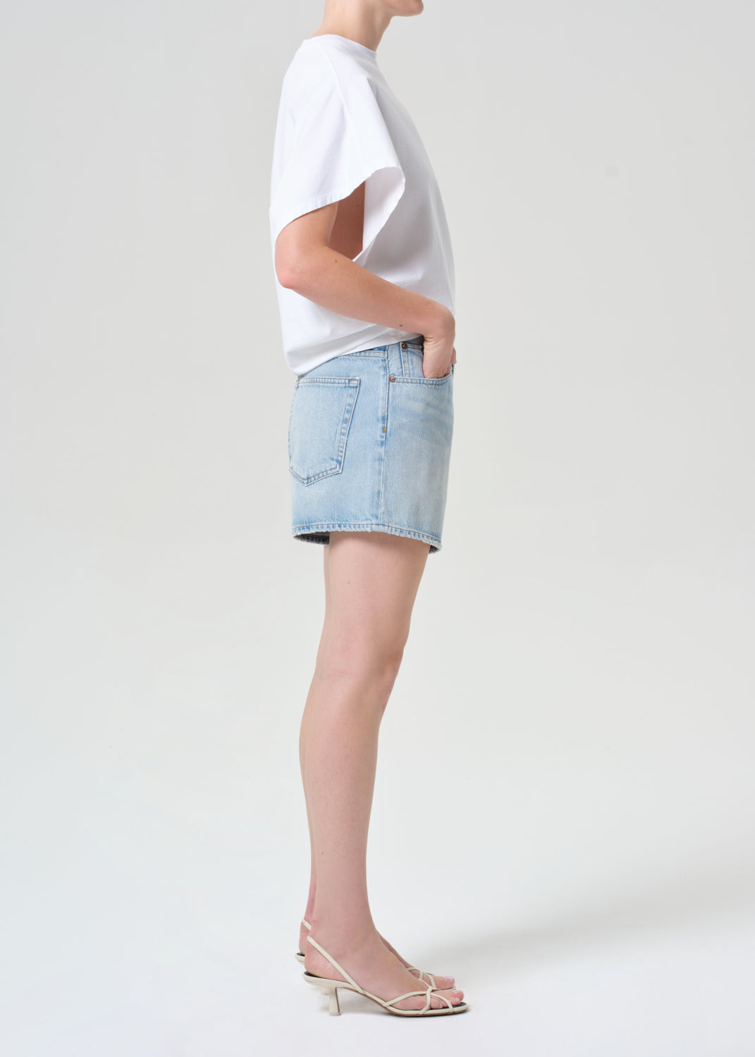 Person wearing a white t-shirt and light blue denim shorts on a plain background