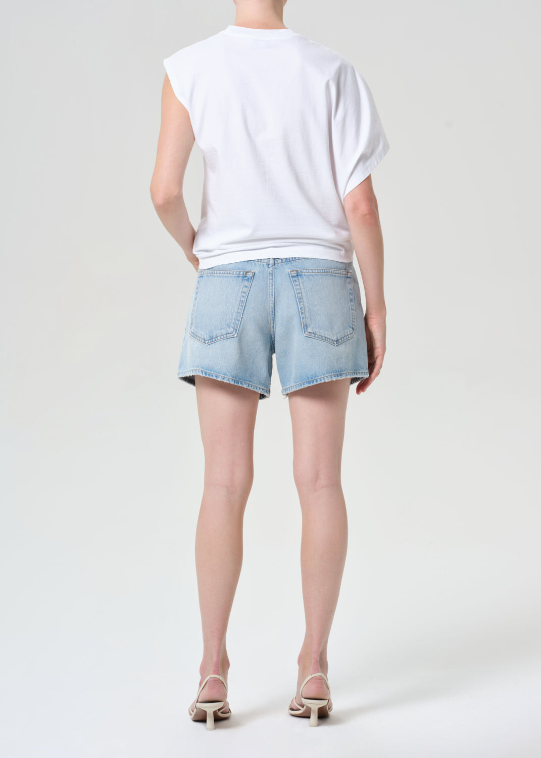 Person wearing a white t-shirt and light blue denim shorts on a plain background
