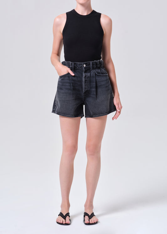 Person wearing black sleeveless top and denim shorts on a white background