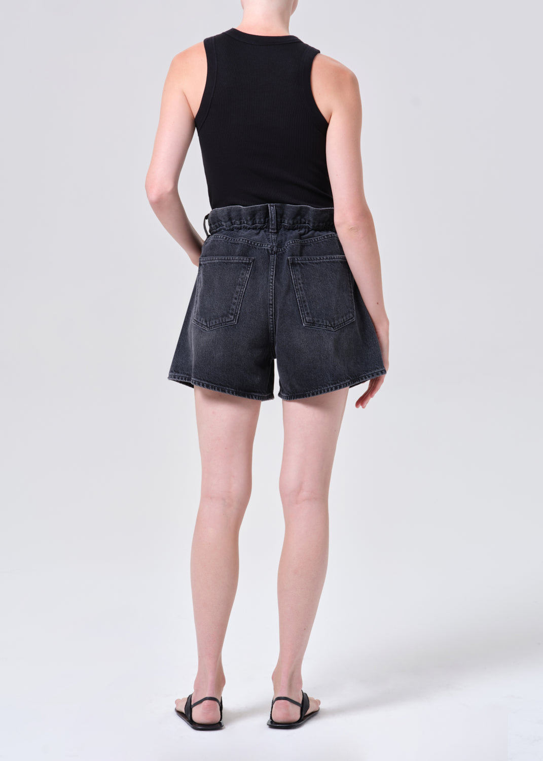 Person wearing black denim shorts and a black sleeveless top on a white background