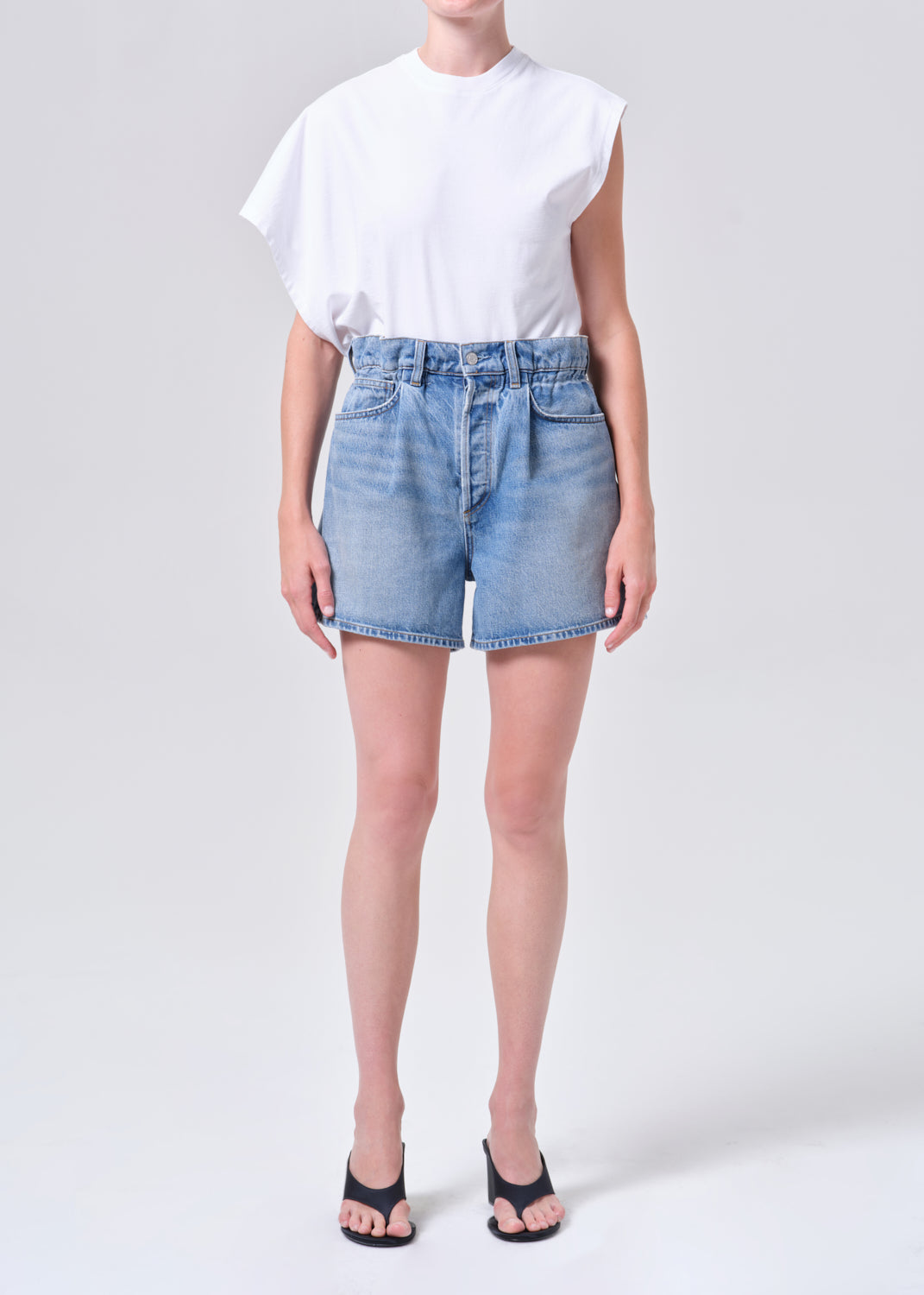 Person wearing a white t-shirt and light blue denim shorts on a plain background