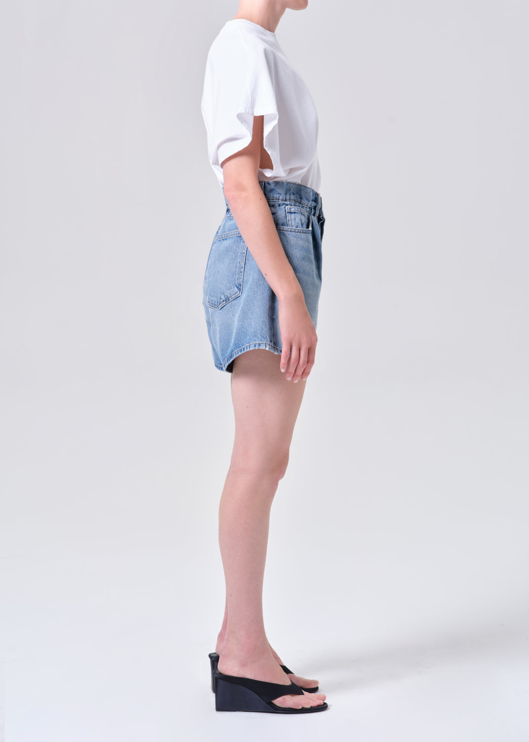 Person wearing a white t-shirt and blue denim shorts on a plain background
