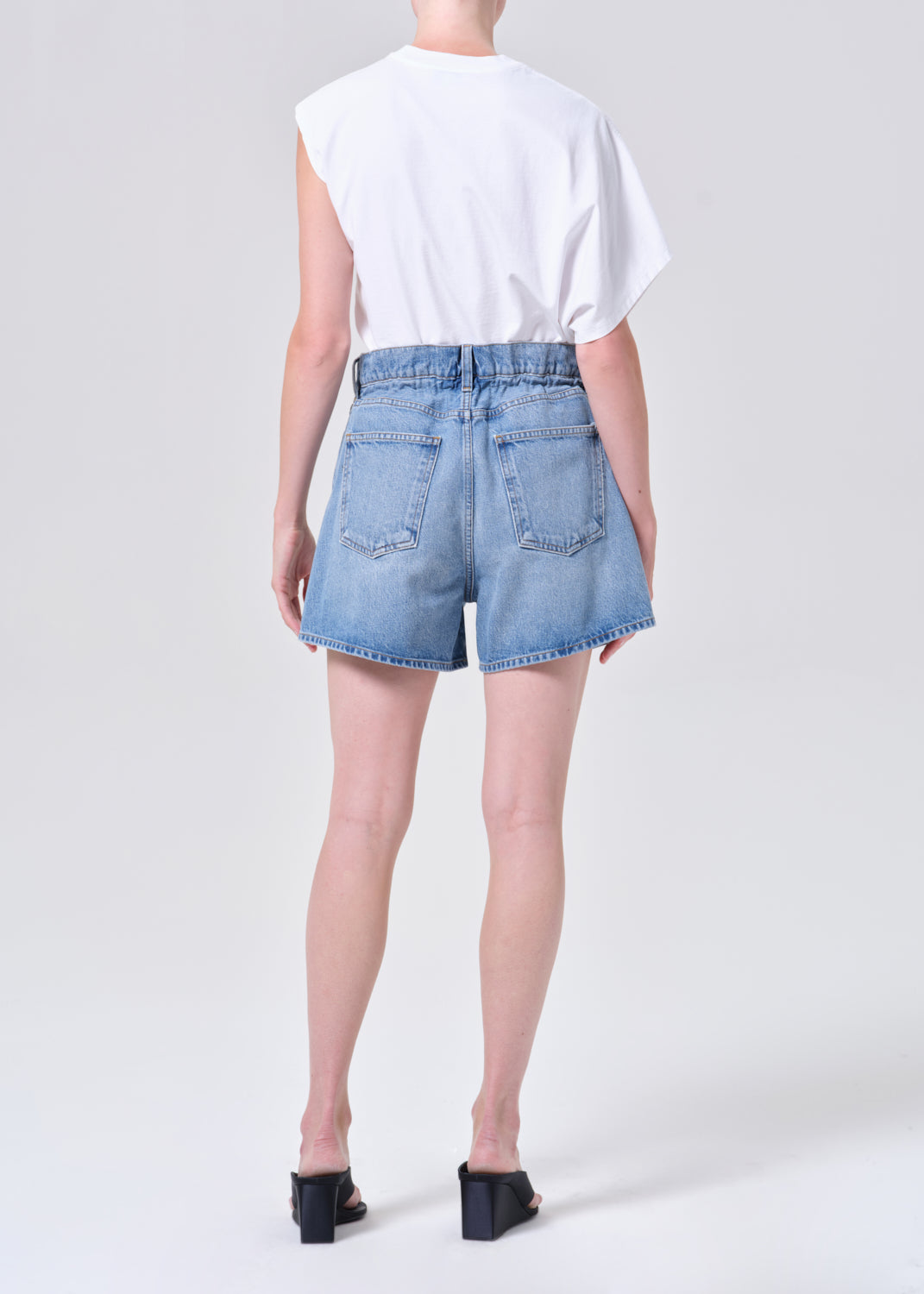 Person wearing light blue denim shorts and a white top on a plain background