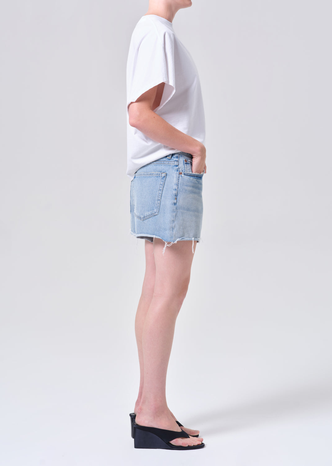 Person wearing a white oversized t-shirt and light blue denim shorts on a plain background