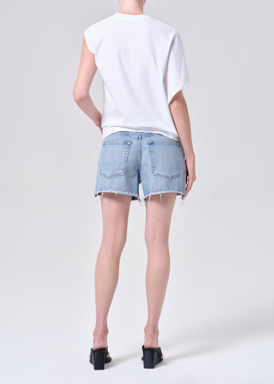 Person wearing a white sleeveless top and light blue denim shorts on a plain background