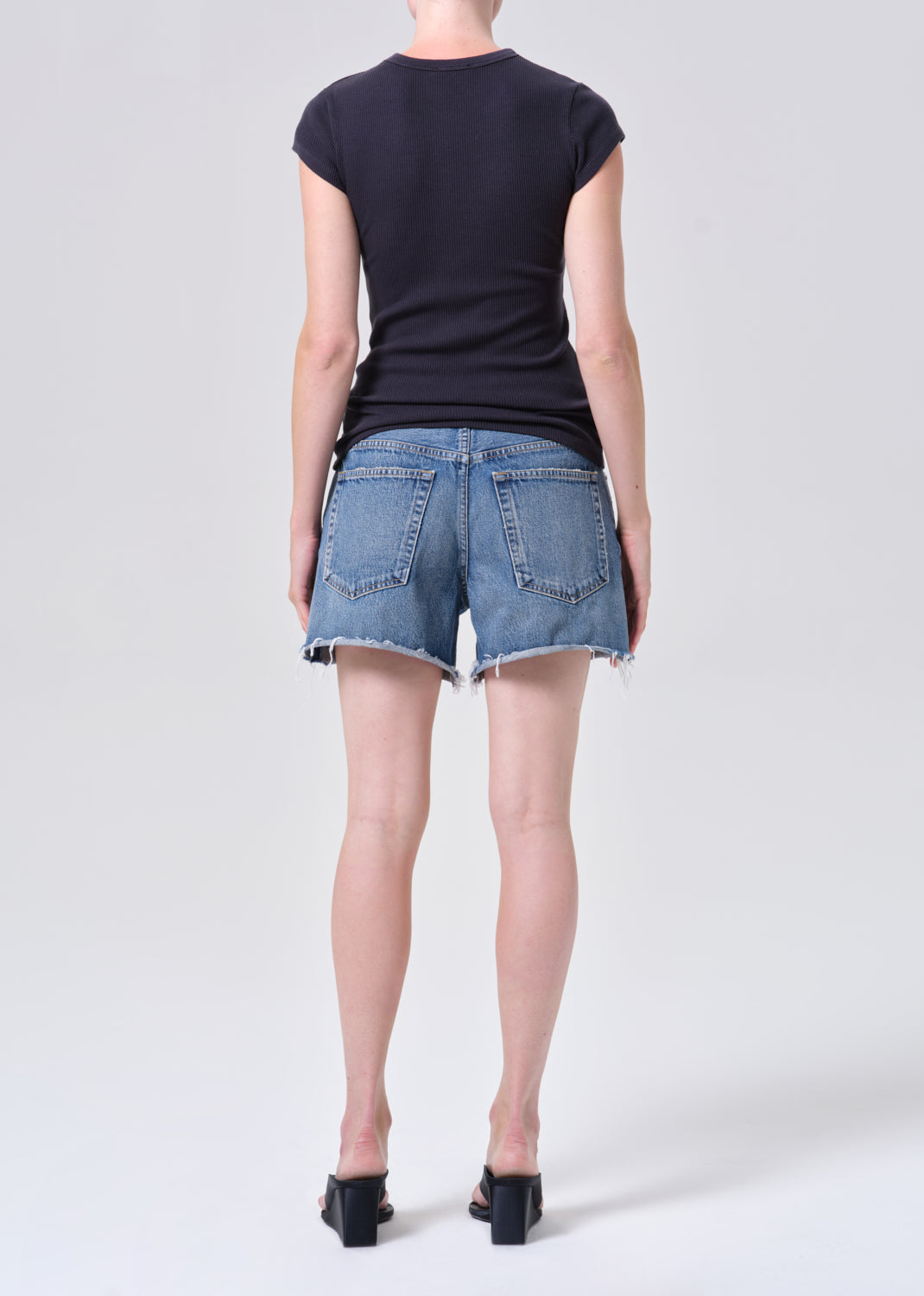 Person wearing a black t-shirt and blue denim shorts on a white background