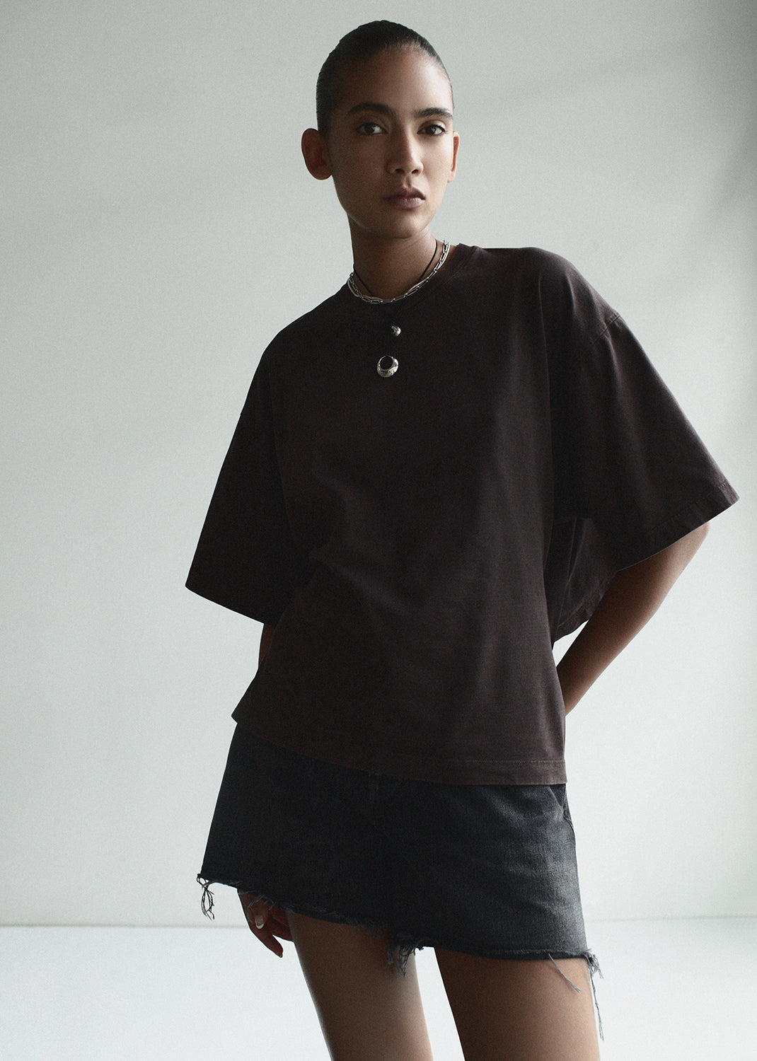 Person wearing a dark brown oversized shirt and black shorts on a plain background
