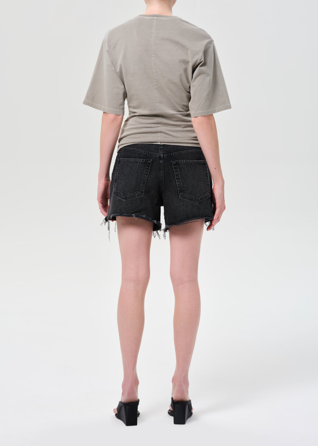 Person wearing a beige t-shirt and black shorts on a white background