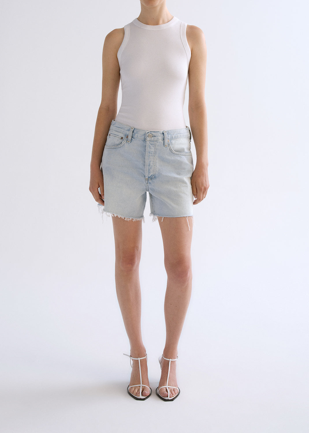 Person wearing white tank top with blue shorts on a grey background