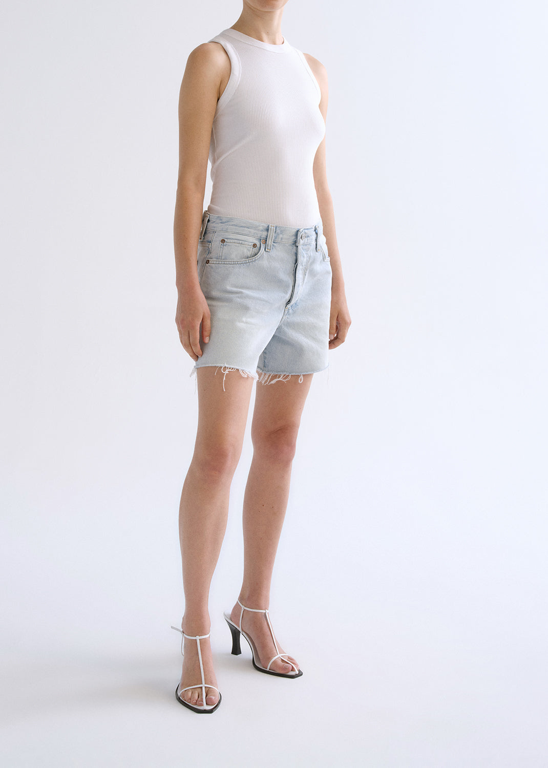 Person wearing white tank top with blue shorts on a grey background