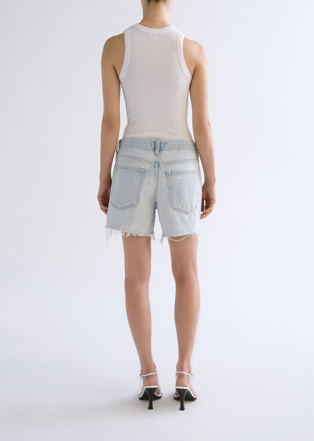 Person wearing white tank top with blue shorts on a grey background
