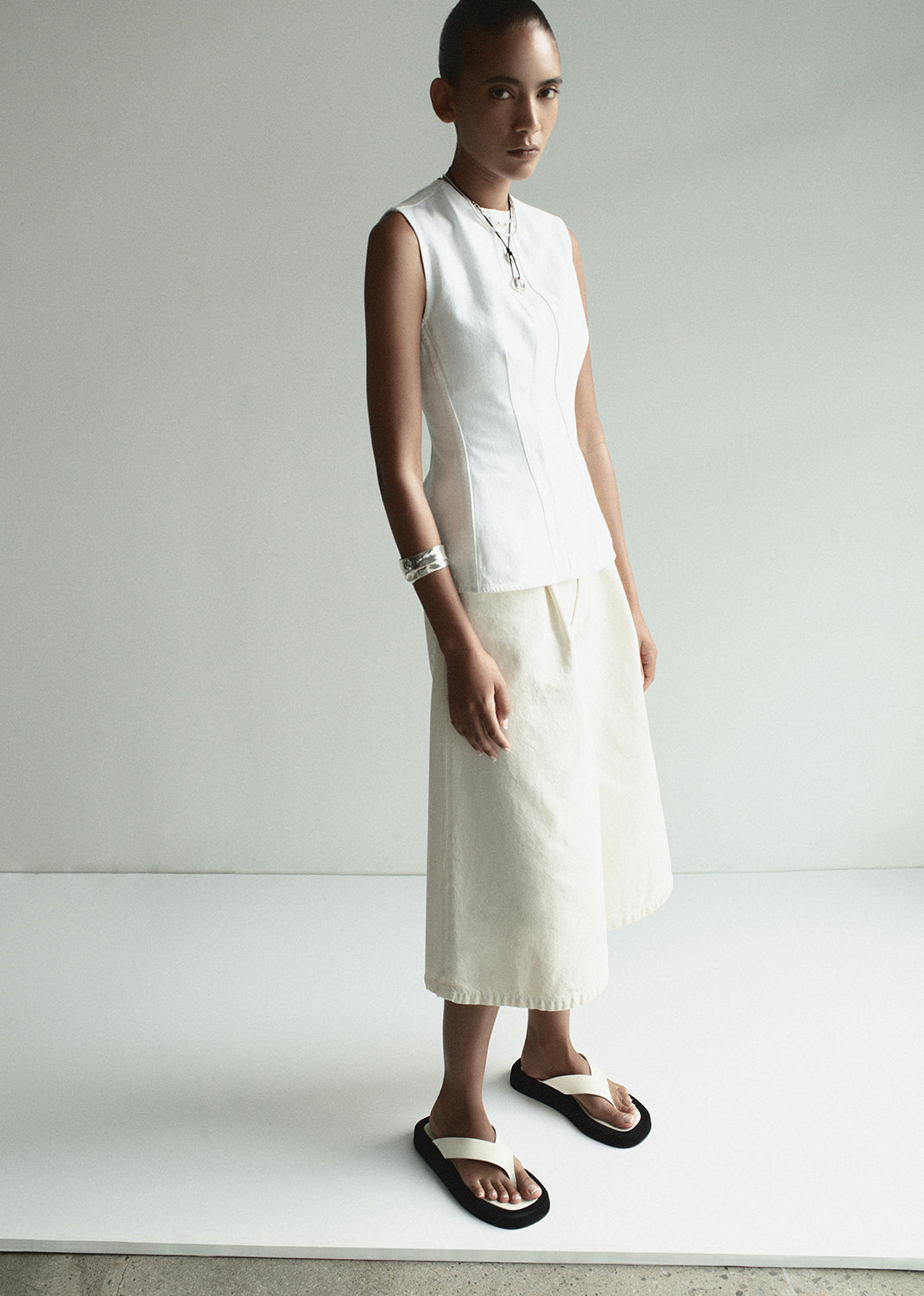Person wearing a white sleeveless top and skirt with black sandals on a plain background