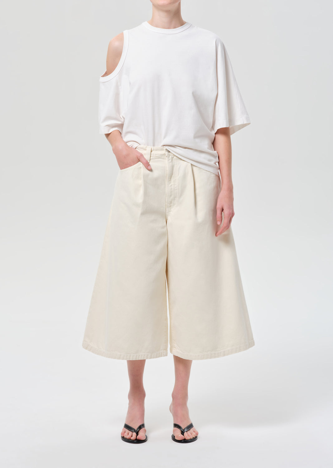 Person wearing a white off-shoulder top and cream-colored wide-leg pants on a plain background