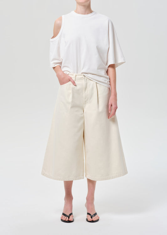 Person wearing a white off-shoulder top and cream-colored wide-leg pants on a plain background