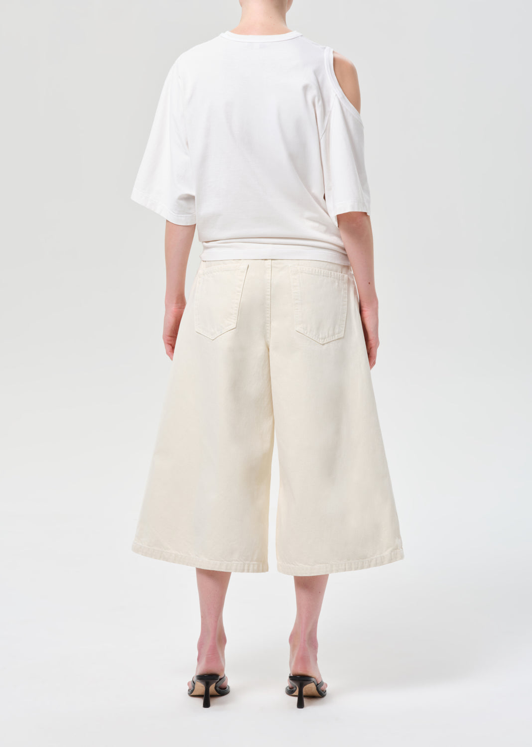 Person wearing a white top and cream-colored wide-leg pants on a white background