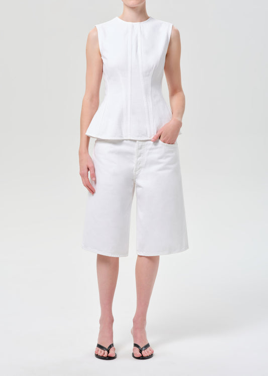 Person wearing a white sleeveless top and white pants on a light gray background