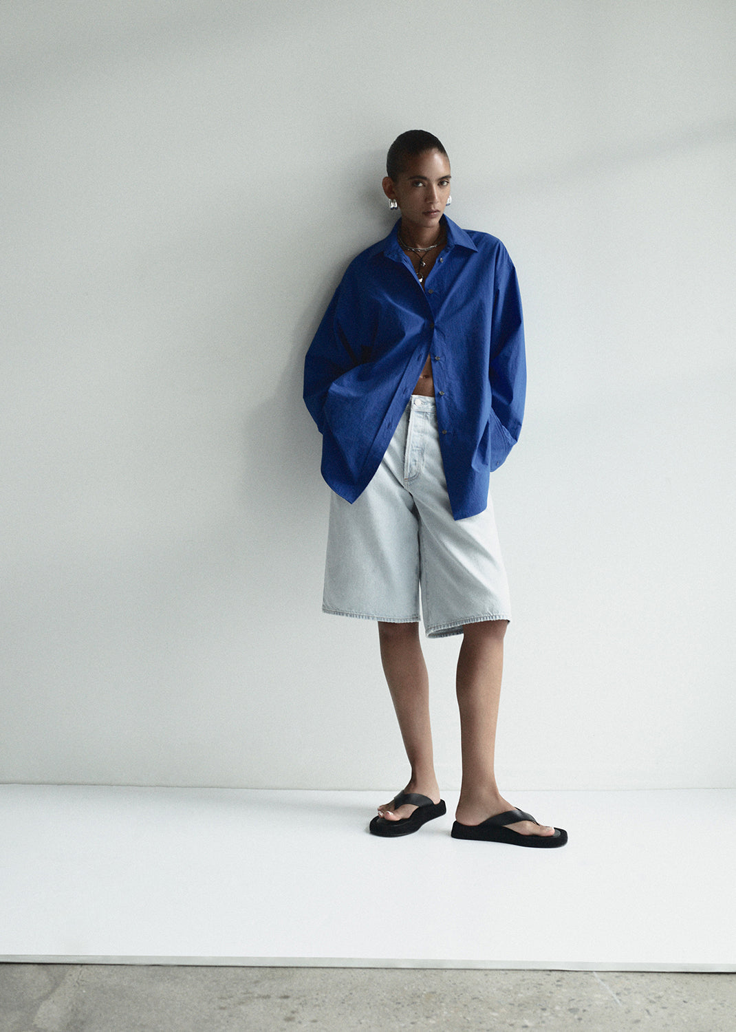 Person wearing a blue oversized shirt and white shorts against a plain background