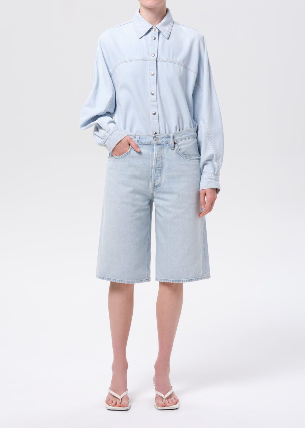 Person wearing a light blue shirt and denim shorts on a white background