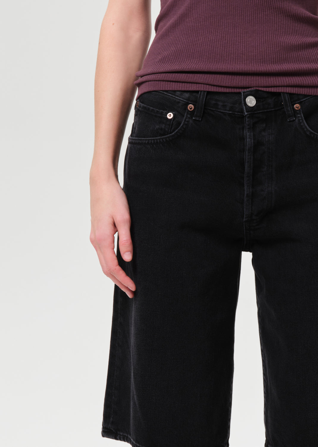 Person wearing black jeans and a maroon top on a white background