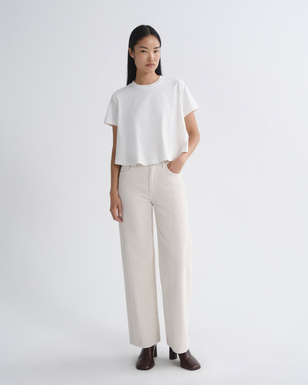 Woman wearing a white t-shirt and beige pants on a plain background