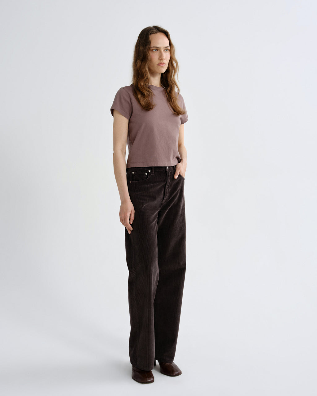 Woman wearing a brown t-shirt and dark pants on a white background