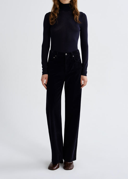 A model wearing a dark navy long-sleeve mock neck top and matching dark navy wide-leg trousers, paired with brown leather shoes, against a grey background.