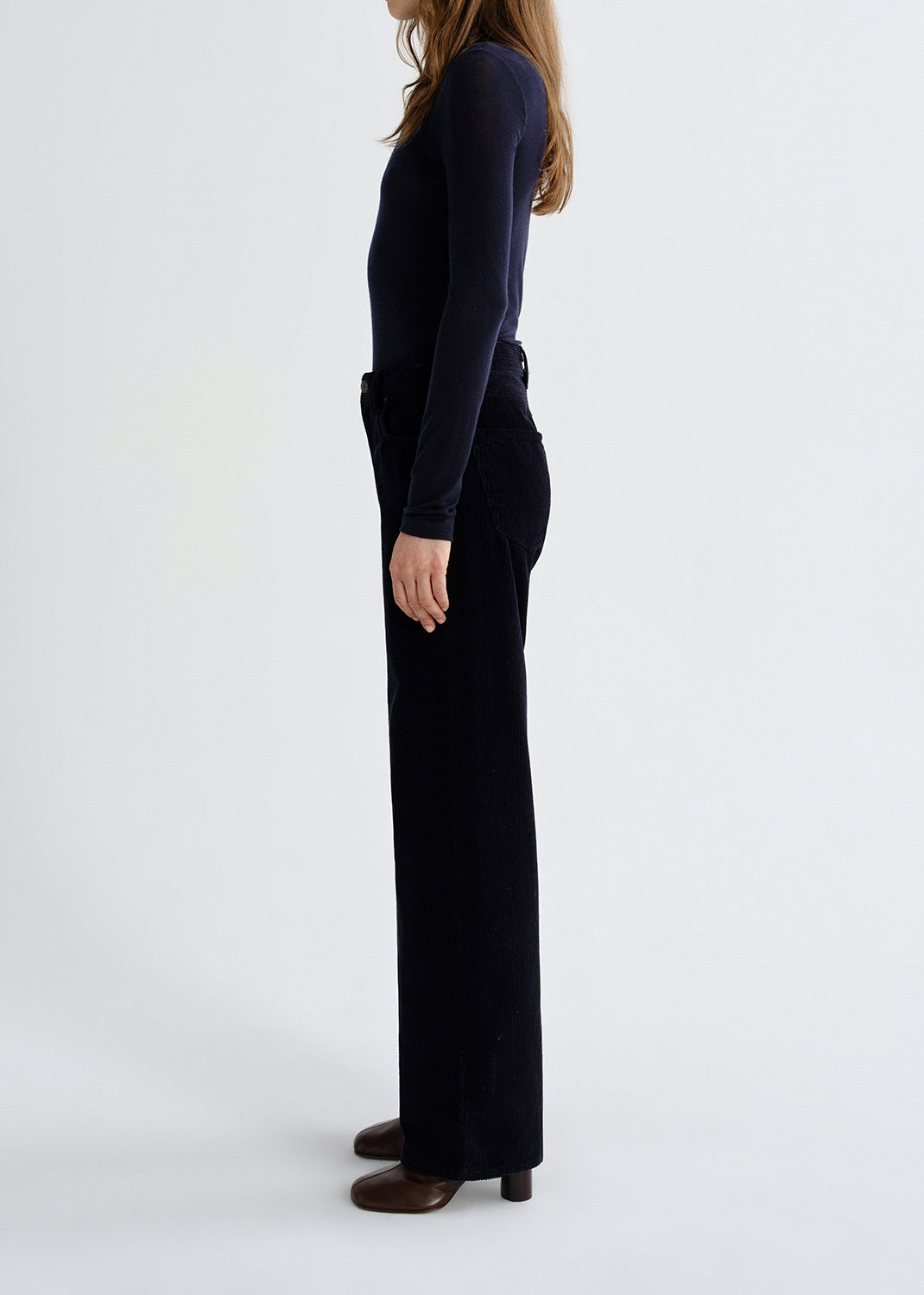 A side-profile view of a model wearing a dark navy long-sleeve top and matching dark navy wide-leg trousers, paired with brown shoes, against a grey background.