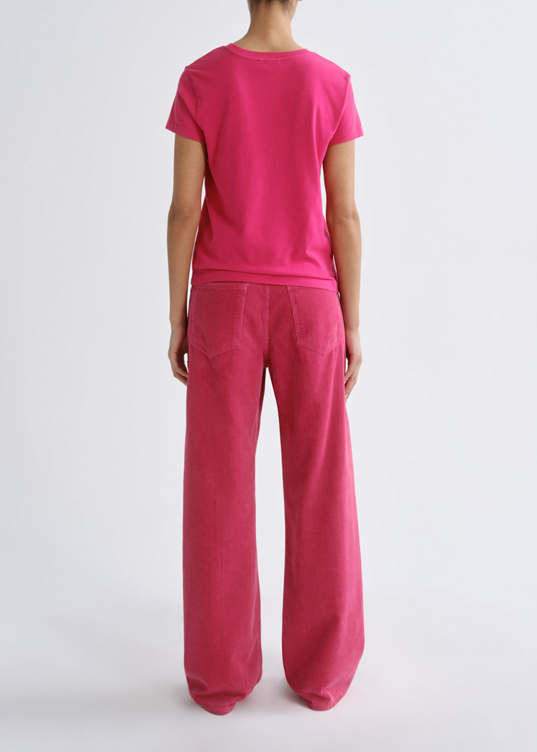 A model shown from the back wearing a bright pink short-sleeve t-shirt and matching wide-leg trousers against a grey background.
