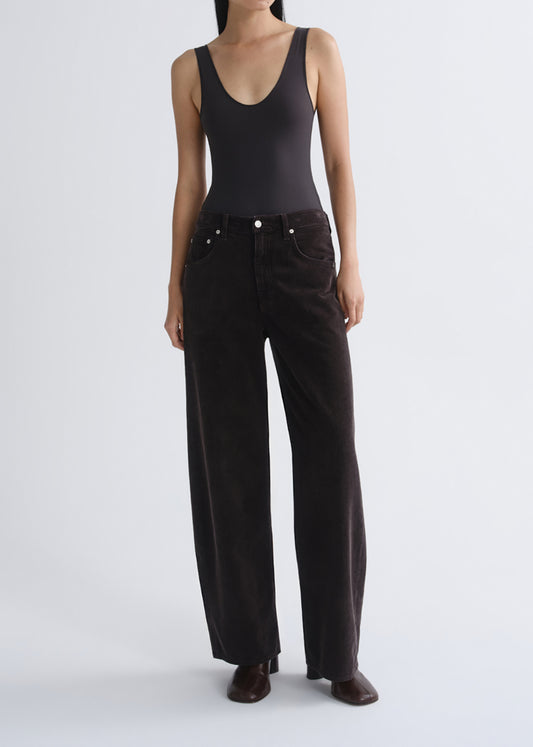A model wearing a black sleeveless bodysuit and black wide-leg corduroy trousers, standing against a grey background.