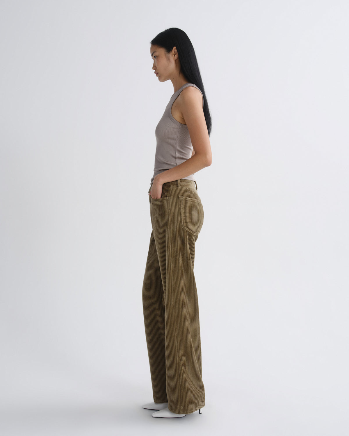 Woman wearing a gray tank top and brown corduroy pants on a grey background