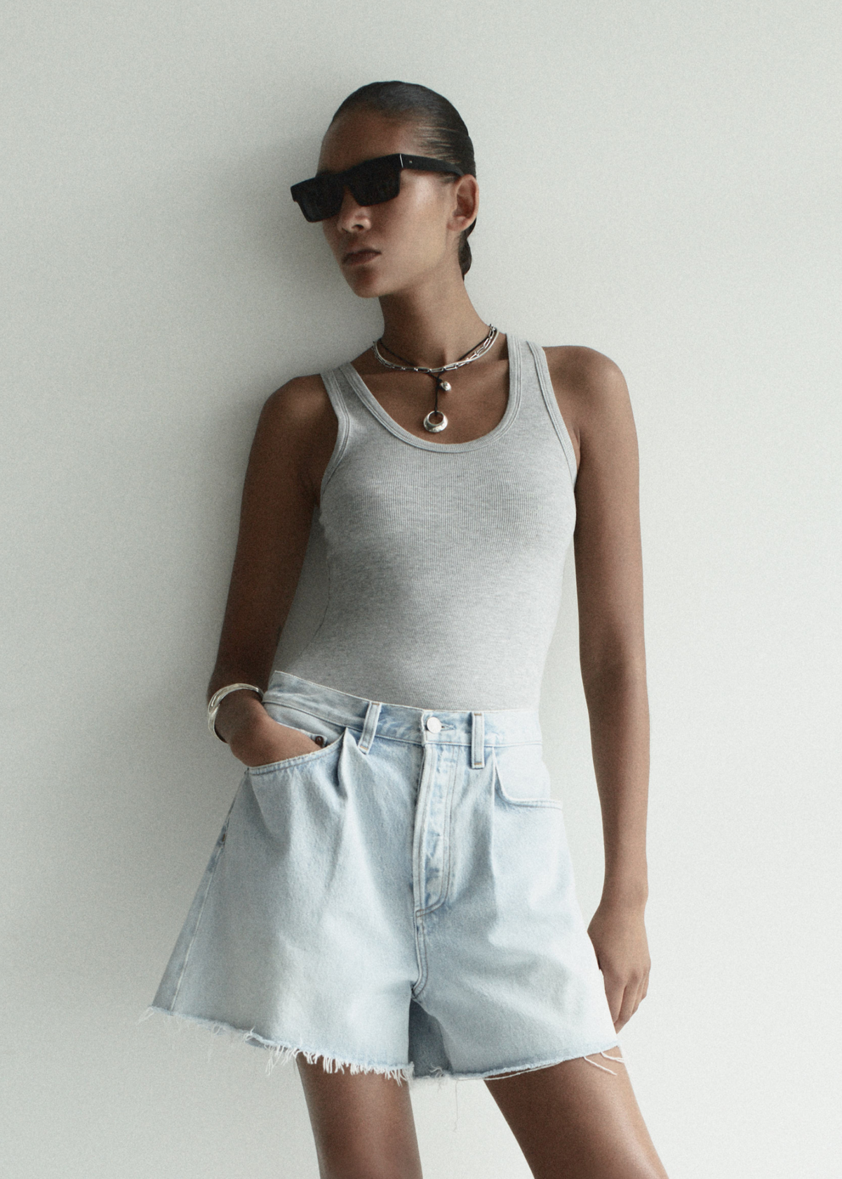 Woman wearing a gray tank top and denim shorts against a plain background