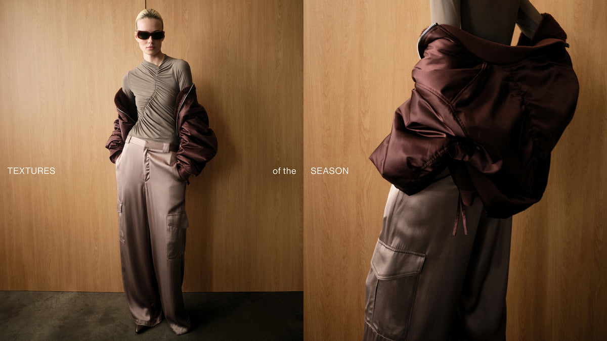 A split-screen fashion editorial image showing a model and a mannequin wearing a textured taupe top, wide-leg taupe trousers, and a dark burgundy satin jacket draped over the shoulders. The background is a warm wood-paneled wall.