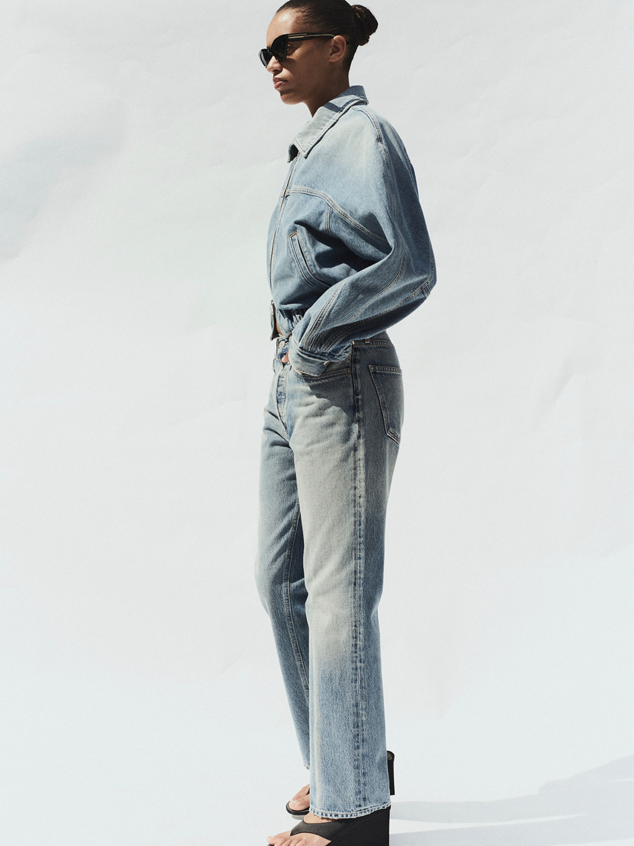 Person wearing a light blue denim jacket and jeans against a white background