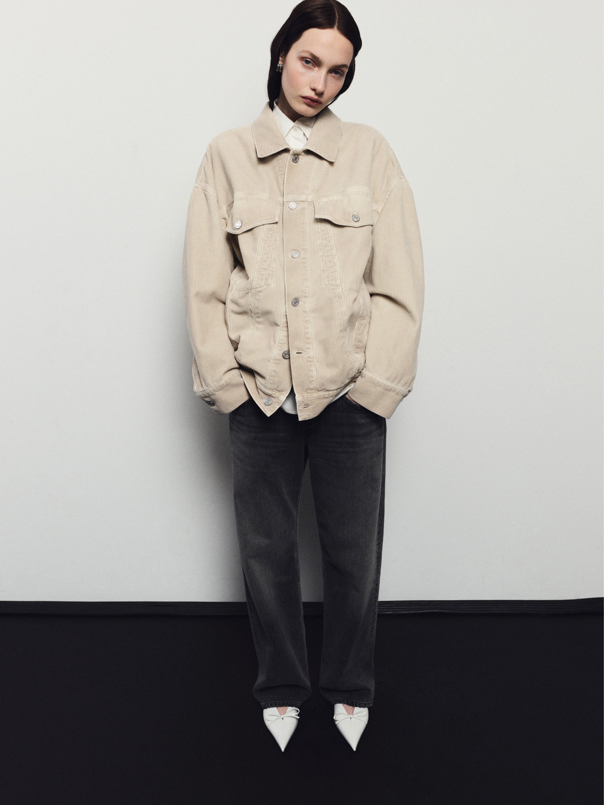 Person wearing a beige jacket and dark pants against a white background