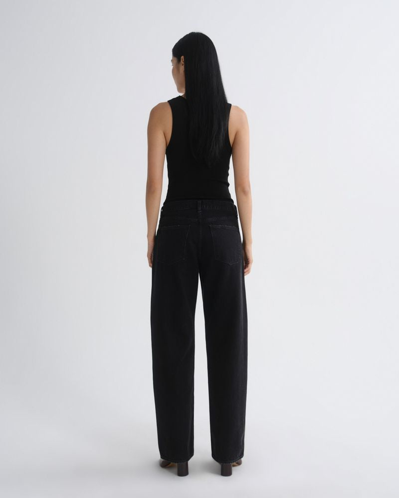 A model viewed from the back wearing a black sleeveless top and black wide-leg jeans against a plain light gray studio background.